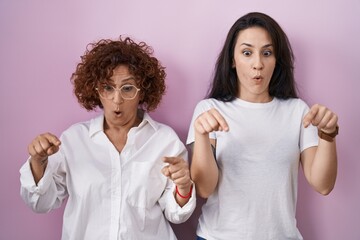 Hispanic mother and daughter wearing casual white t shirt over pink background pointing down with fingers showing advertisement, surprised face and open mouth