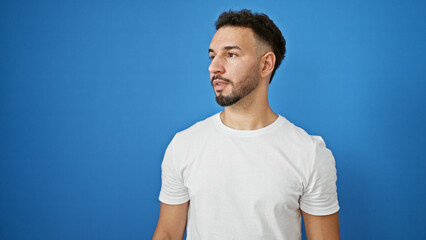 Young arab man looking to the side with serious expression over isolated blue background