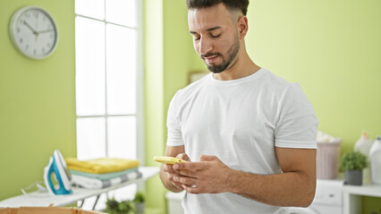 Young arab man using smartphone smiling at laundry room