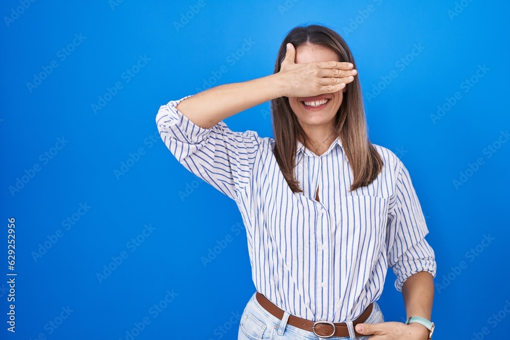 Canvas Prints Hispanic young woman standing over blue background smiling and laughing with hand on face covering eyes for surprise. blind concept.