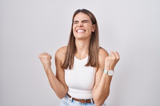 Hispanic young woman standing over white background very happy and excited doing winner gesture with arms raised, smiling and screaming for success. celebration concept.