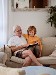 Boy and grandfather reading book on couch during free time