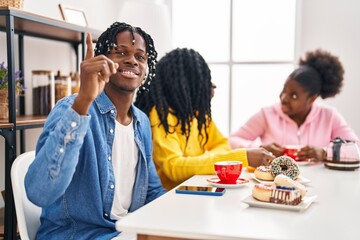 Fototapeta na wymiar Group of three young black people sitting on a table having coffee surprised with an idea or question pointing finger with happy face, number one