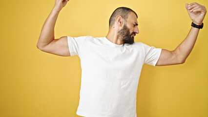 Young hispanic man doing strong gesture with arms over isolated yellow background