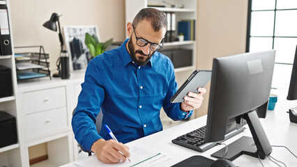 Young hispanic man business worker using touchpad taking notes at office