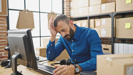 Young hispanic man ecommerce business worker using computer stressed at office