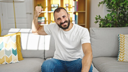 Young hispanic man smiling confident doing strong gesture with arm at home