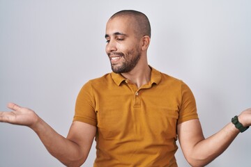Hispanic man with beard standing over white background smiling showing both hands open palms,...