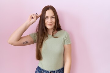 Beautiful brunette woman standing over pink background smiling pointing to head with one finger, great idea or thought, good memory