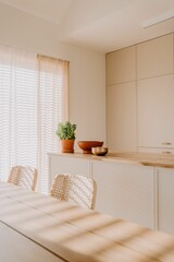 Modern dining room featuring light-colored furniture and a large window with blinds