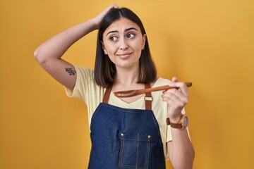 Hispanic girl eating healthy  wooden spoon confuse and wondering about question. uncertain with...