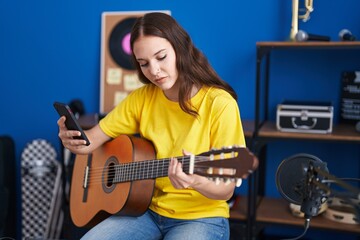 Fototapeta na wymiar Young woman musician playing classical guitar using smartphone at music studio
