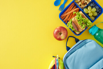 Nourishing snack selection for school concept. Top view shot of food container, water bottle, apple, schoolbag, pencil case, pen, cutlery on yellow background with empty space for promo or text