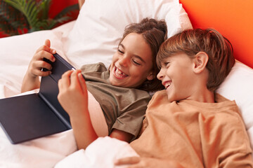 Adorable boys using touchpad lying on bed at bedroom