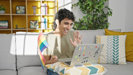 Young hispanic man holding rainbow flag having video call at home