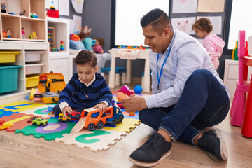Hispanic man with boy and girl playing with car toy sitting on floor at kindergarten