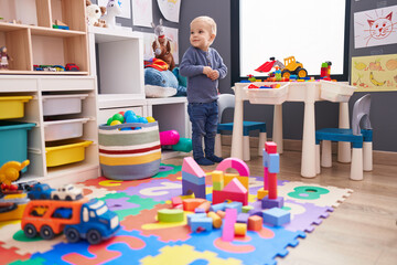 Adorable caucasian boy playing with construction blocks standing at kindergarten