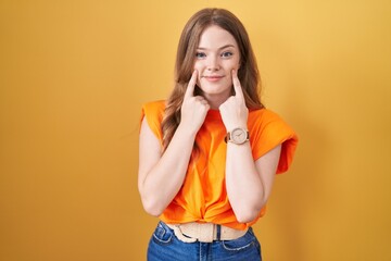 Caucasian woman standing over yellow background smiling with open mouth, fingers pointing and...