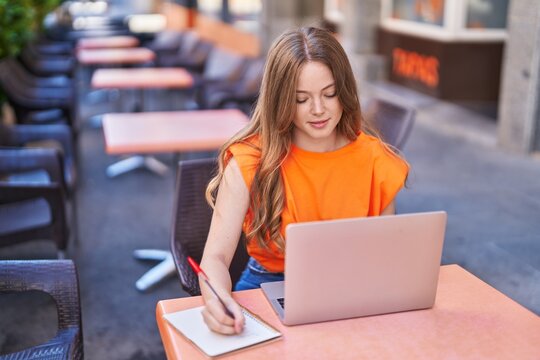 Young woman using laptop writing on notebook at coffee shop terrace