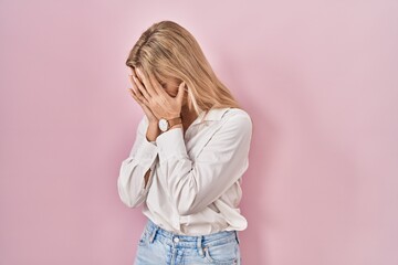 Young caucasian woman wearing casual white shirt over pink background with sad expression covering...