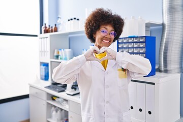 Young african american woman working at scientist laboratory smiling in love doing heart symbol shape with hands. romantic concept.
