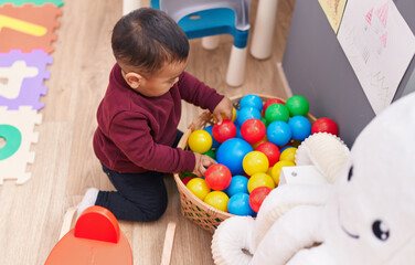 Fototapeta na wymiar Adorable hispanic boy playing with balls sitting on floor at kindergarten