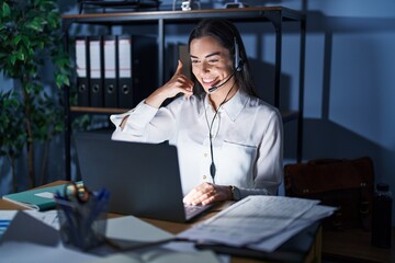 Young brunette woman wearing call center agent headset working late at night smiling doing phone...