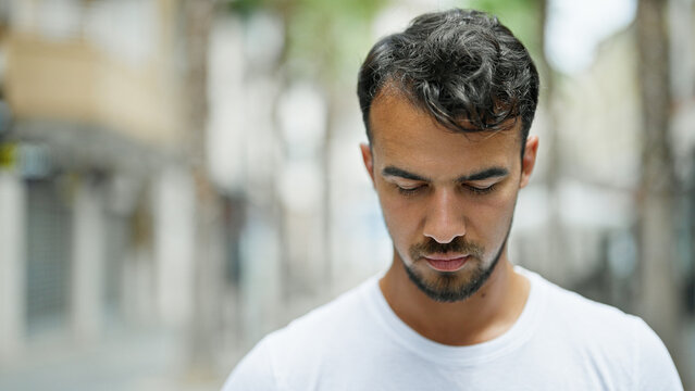 Young hispanic man looking down with serious expression at street