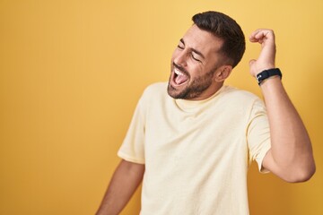 Handsome hispanic man standing over yellow background dancing happy and cheerful, smiling moving casual and confident listening to music