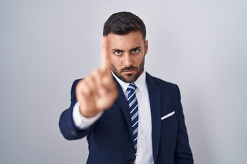 Handsome hispanic man wearing suit and tie pointing with finger up and angry expression, showing no gesture