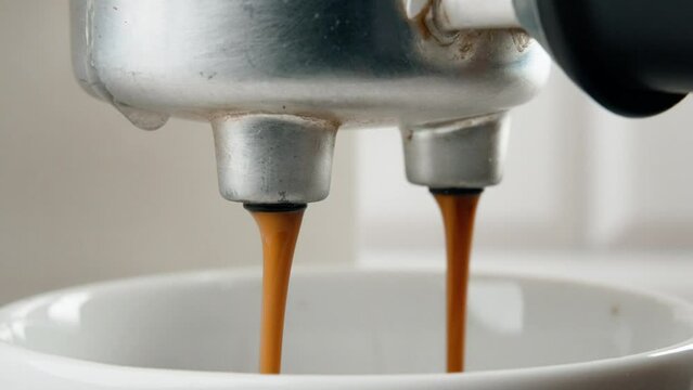 Close-up slow-motion view of pouring espresso in a cup from a coffee machine