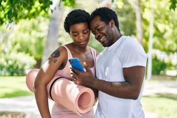 African american man and woman couple holding yoga mat using smartphone at park