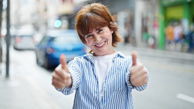 Middle age woman smiling confident doing ok sign with thumbs up at street