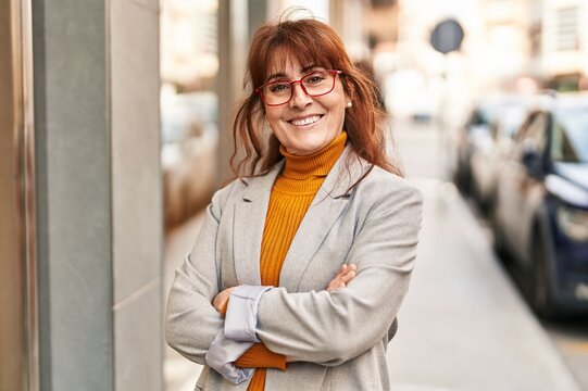 Middle age woman business executive standing with arms crossed gesture at street