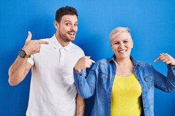 Young brazilian mother and son standing over blue background looking confident with smile on face, pointing oneself with fingers proud and happy.