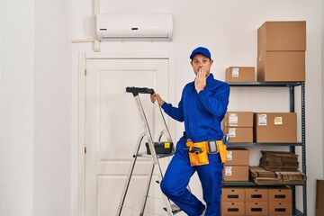 Young hispanic man working at renovation covering mouth with hand, shocked and afraid for mistake. surprised expression
