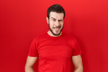 Fototapeta premium Young hispanic man wearing casual red t shirt winking looking at the camera with sexy expression, cheerful and happy face.