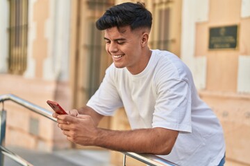 Young hispanic man smiling confident using smartphone at street