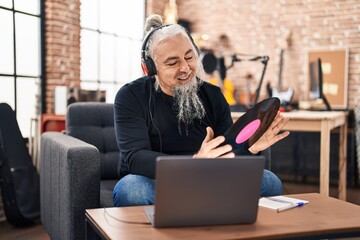 Middle age grey-haired man musician listening to music holding vinyl disc at music studio