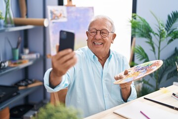 Senior grey-haired man artist smiling confident make selfie by smartphone at art studio