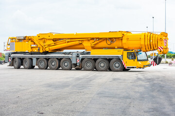 Obraz premium Mobile cranes 500 ton construction cranes with yellow telescopic arms and big tower cranes in sunny day with white clouds and deep blue sky on background, heavy industry port