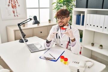 Young arab man wearing doctor uniform analysing urine test tube speaking at clinic