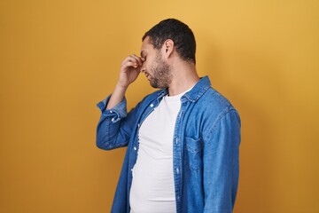 Hispanic man standing over yellow background tired rubbing nose and eyes feeling fatigue and headache. stress and frustration concept.