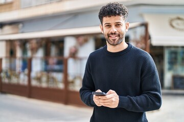 Young arab man smiling confident using smartphone at street