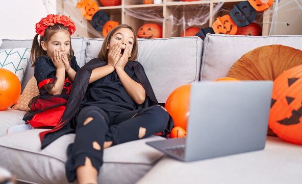 Adorable boy and girl wearing halloween costume watching movie on laptop with terrified expression at home