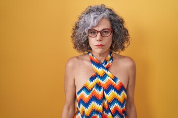 Middle age woman with grey hair standing over yellow background skeptic and nervous, frowning upset...