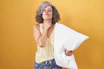 Middle age woman with grey hair wearing pijama hugging pillow touching painful neck, sore throat...