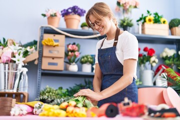 Young blonde girl florist make bouquet of flowers cutting stem at florist