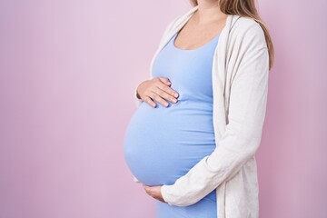 Young pregnant woman expecting a baby, touching pregnant belly looking positive and happy standing...