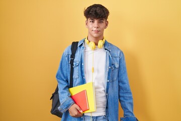 Hispanic teenager wearing student backpack and holding books winking looking at the camera with...